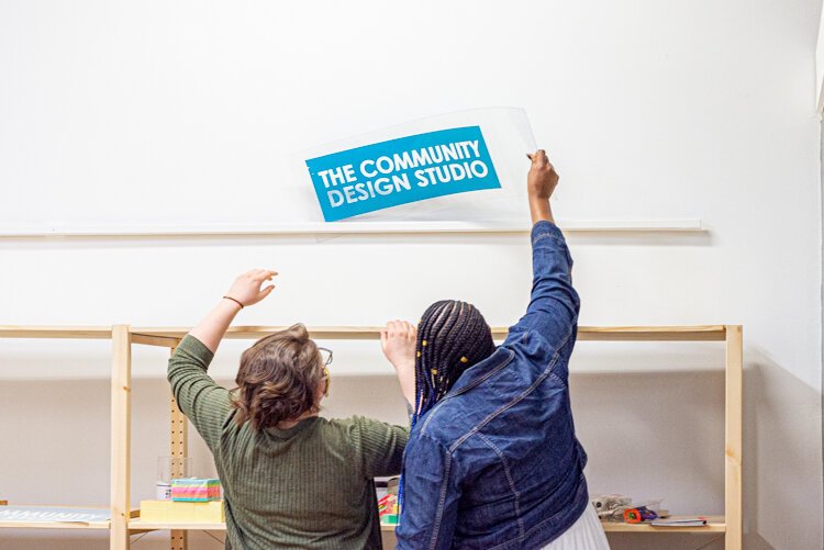 Ru Hensly and Salina Johnson work with the sign for The Community Design Studio.