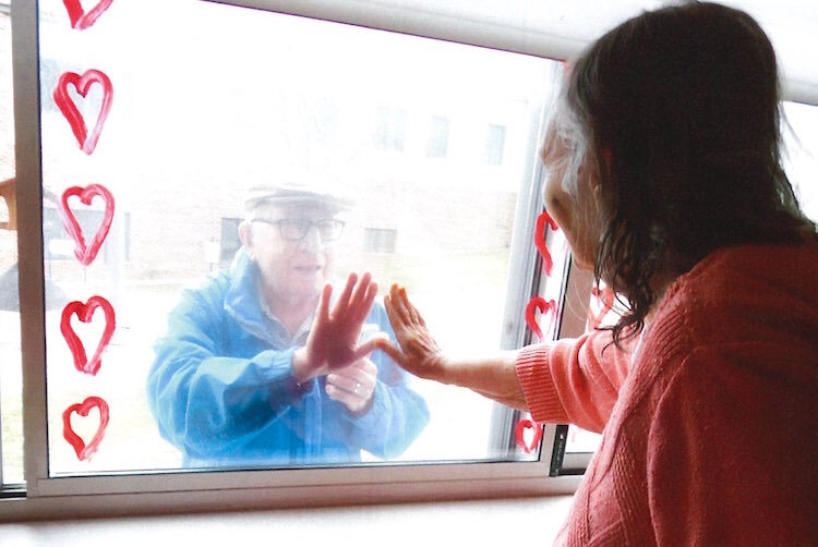 A man touches the glass outside a room of a loved one at the Heritage Community of Kalamazoo. “Window visits” have become daily events for family members of some senior residents there.