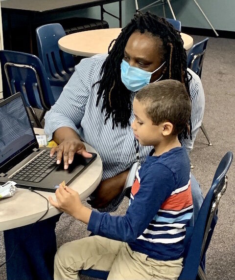 An instructor helps in early elementary student with an online class in New Genesis Academic Hub.