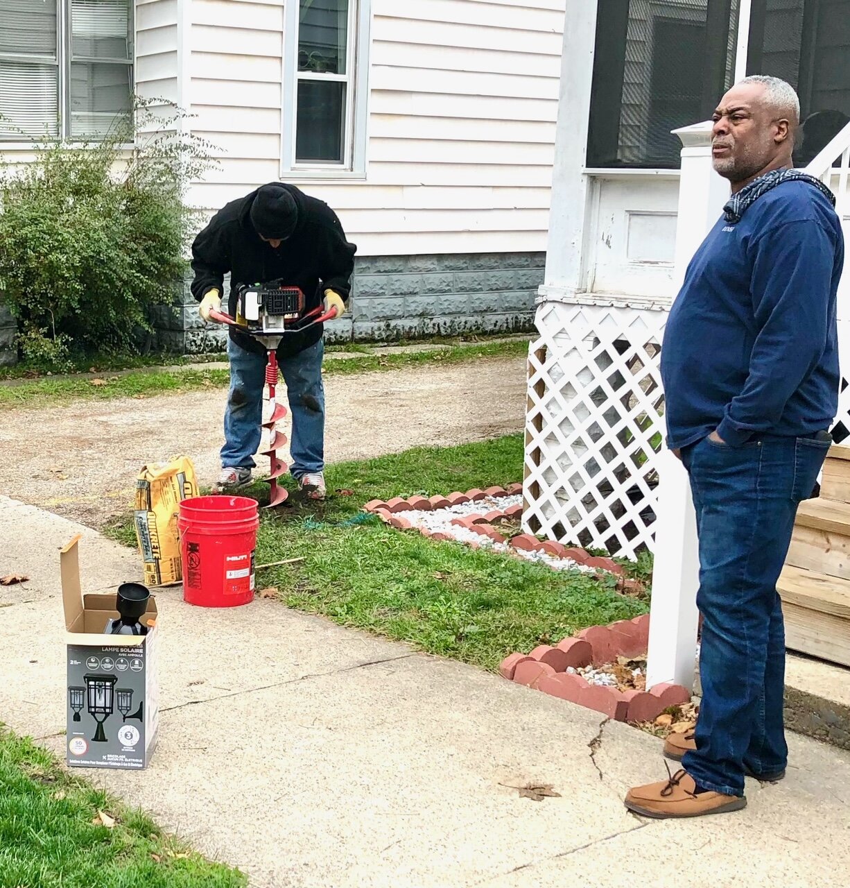 Damion Henderson uses a post hole digger to begin the installation of a solar lamp post in front of the Mabel Street home of Richard Cox IV, at right. The men were photographed as the solar lighting project began in fall of 2020.