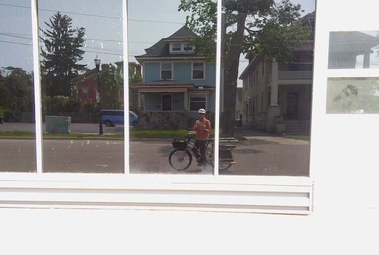 Nora Hauk captures herself on her new cargo e-bike, reflected in a window. Hauk lives on West Main Hill, and prefers to ride on quiet neighborhood streets.
