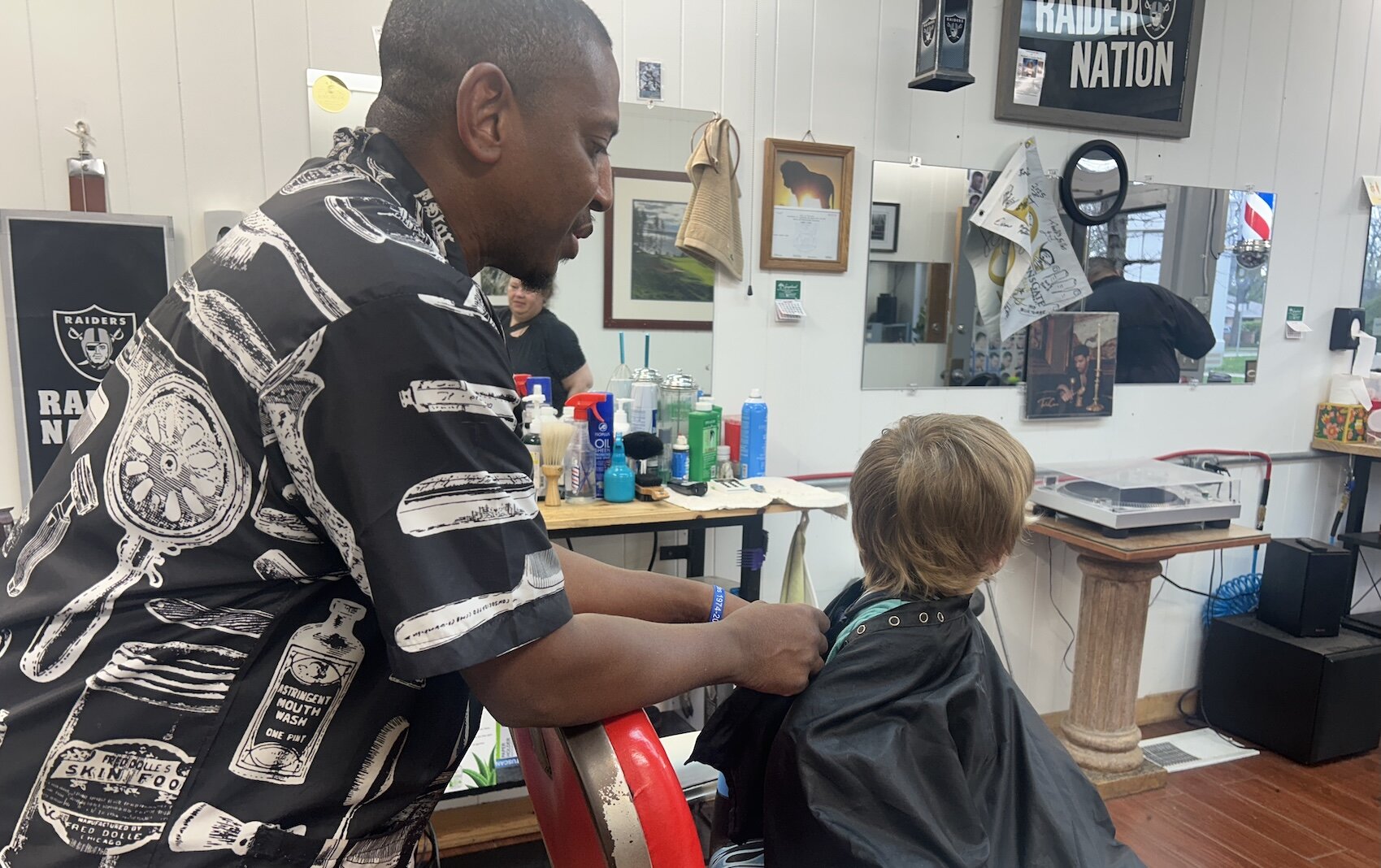 Barber Jerone Lenzy at Rob’s Barber Shop preps a young boy to get his hair cut during a Barbershop and Literacy event in the Vine Neighborhood. 