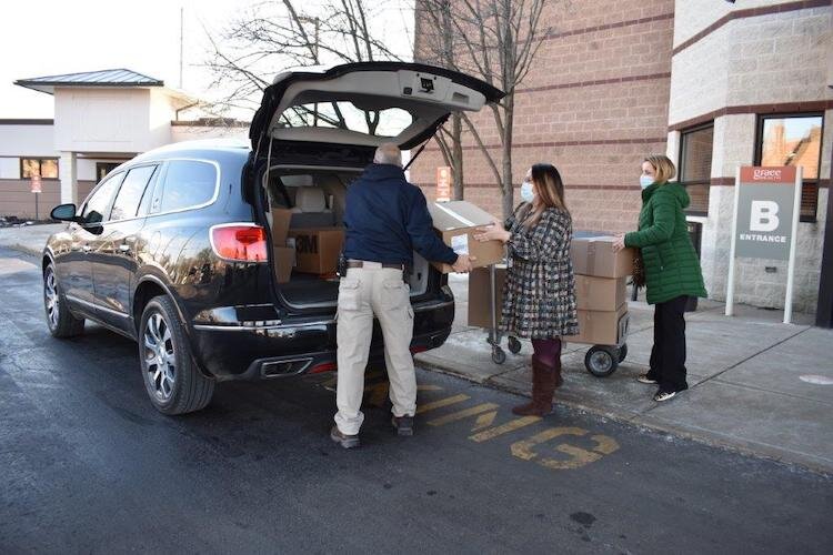 Jessica Gerteisen, center, Risk Management Specialist for Grace Health and Angela Stewart, to her right, Community Initiatives Officer for the Battle Creek Community Foundation, help Keith Crum, a Grace health employee load cases of COVID-19 test kit