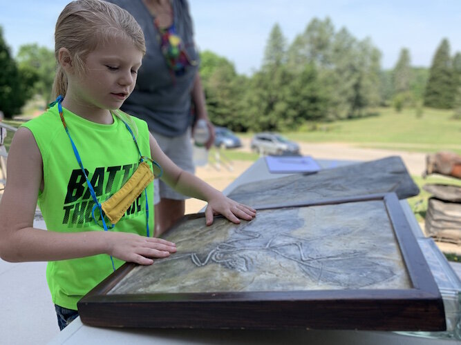 A participant in the outdoor Summer Science camps held every Wednesday examines a fossil imprint on tile.