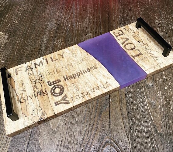A custom designed charcuterie board is shown. It marries yellow birch wood with purple epoxy.