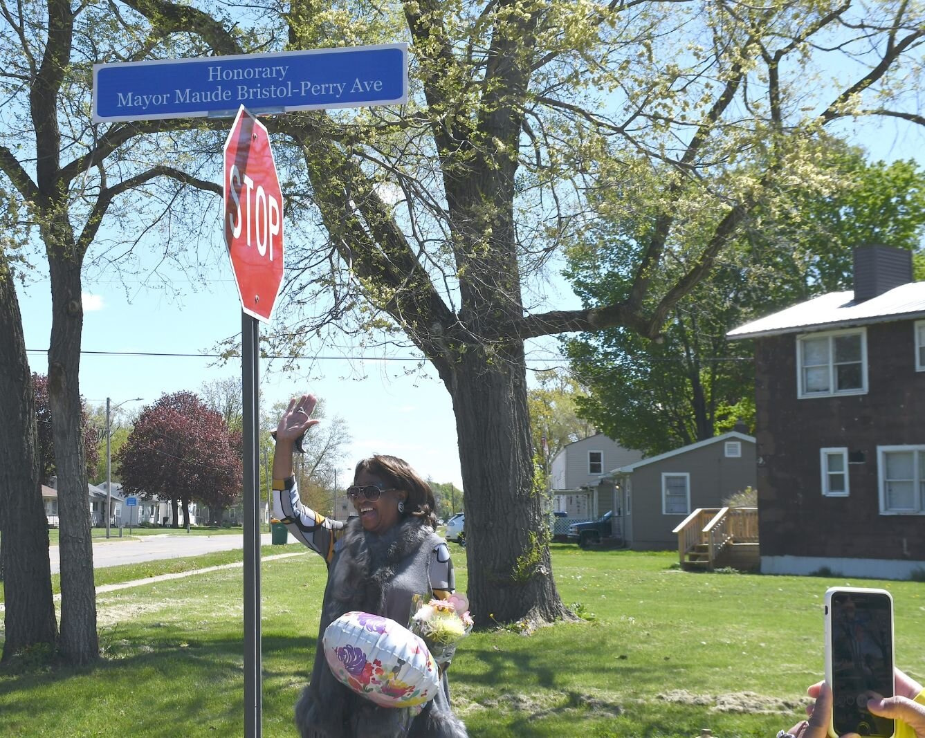 Maude Bristol-Perry stands by the street sign of Honorary Mayor Maude Bristol-Perry Avenue and waves to wellwishers