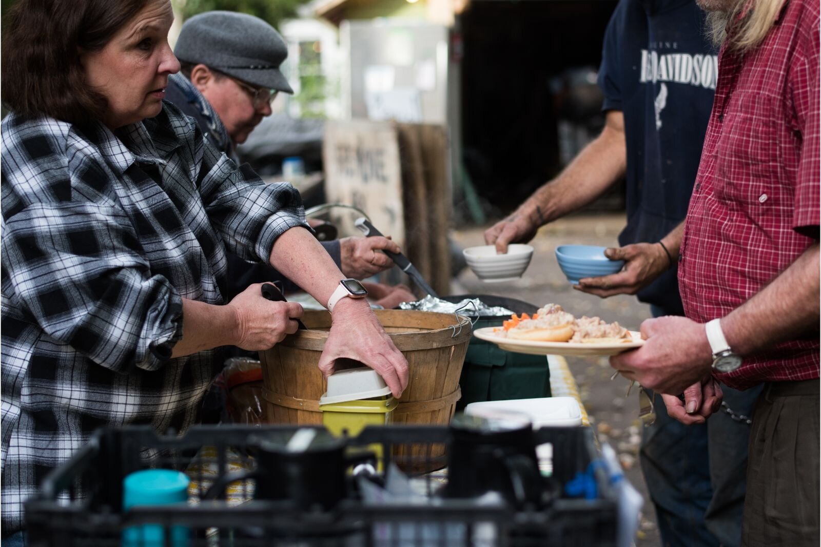 At a dinner for the unsheltered, one of the homeowners says "we provide basic infrastructure for the unhoused community in the area." They have an outdoor kitchen, charging station, an "impromptu warming shelter," refrigerator, sink, and more.