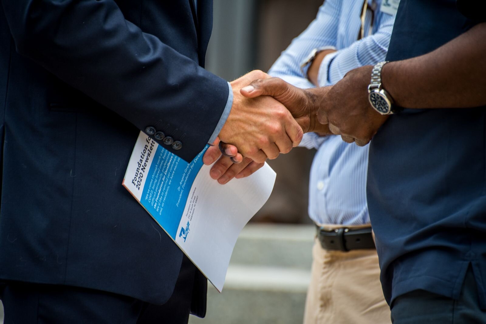 Participants in a press conference to announce a $400 million donation to the Foundation for Excellence exchange a handshake.