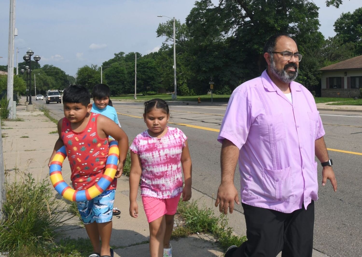 Jose Orozco, executive director of VOCES, walks with a group of children toward a bus stop. The children were going to learn to ride a Battle Creek city bus on their way to Full Blast.
