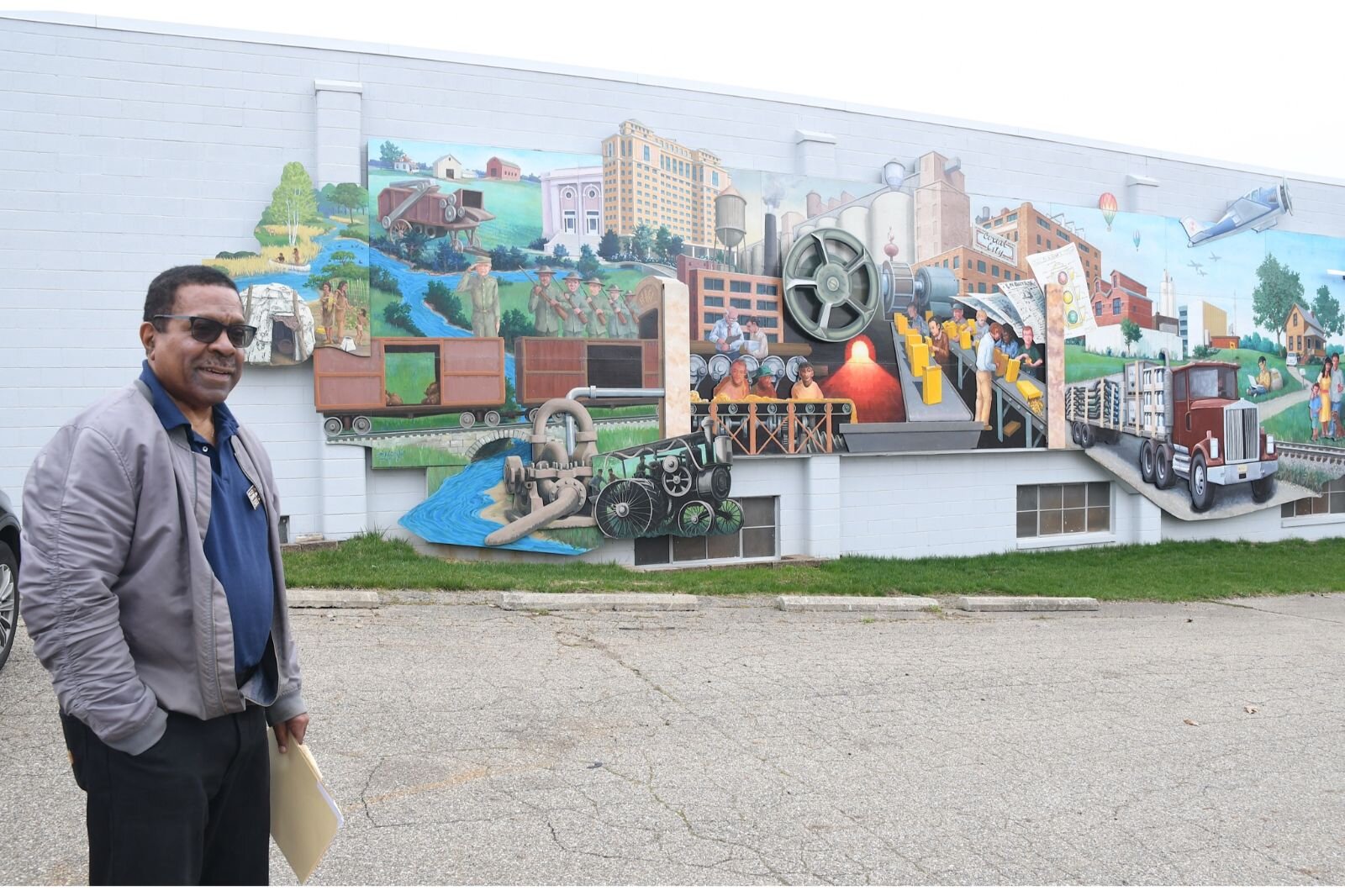 Doug Sturdivant, president of the Regional History Museum Battle Creek Board of Directors, stands by a mural depicting the history of Battle Creek outside of the museum. The mural was donated by Battle Creek Unlimited.
