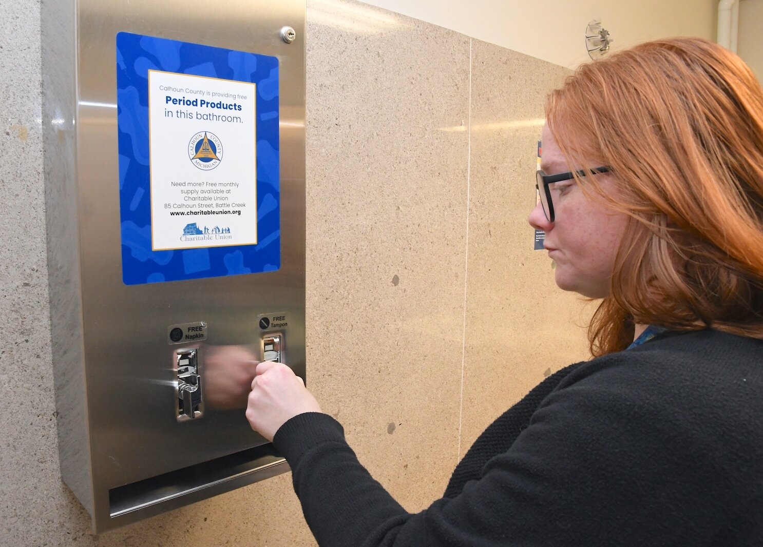 Lucy Blair, Communications Director for Calhoun County, shows how feminine hygiene products dispenser works in a women’s restroom at the Calhoun County building in Marshall.