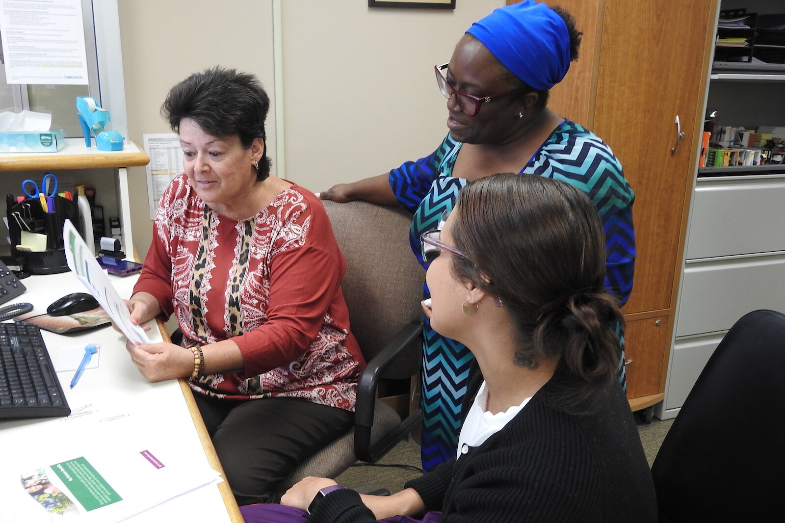 Elishae Johnson, directora de sistema de servicios de salud empresarial en Bronson Healthcare, consulta con la Especialista Administrativa Pam Milliron, a la izquierda, y la Especialista en Información Lexi King en Bronson Battle Creek Psiquiatría y 