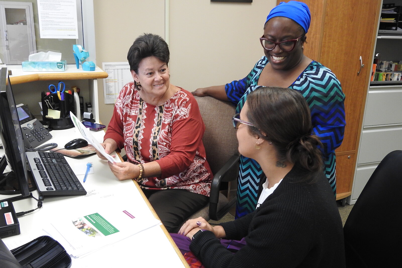 Elishae Johnson, directora de sistema de servicios de salud empresarial en Bronson Healthcare, consulta con la Especialista Administrativa Pam Milliron, a la izquierda, y la Especialista en Información Lexi King en Bronson Battle Creek Psiquiatría y 