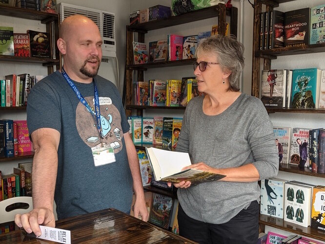 Tom Batterson and customer Laura Webb chat together inside his cargo container store, New Story Community Books.  