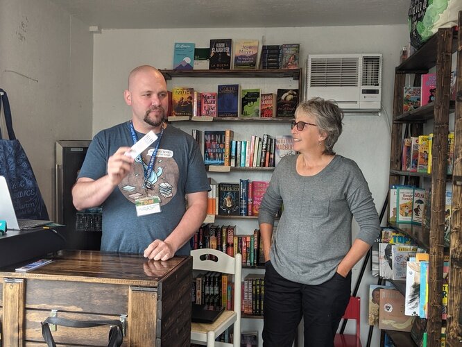 Tom Batterson and customer Laura Webb chat together inside his cargo container store, New Story Community Books.  