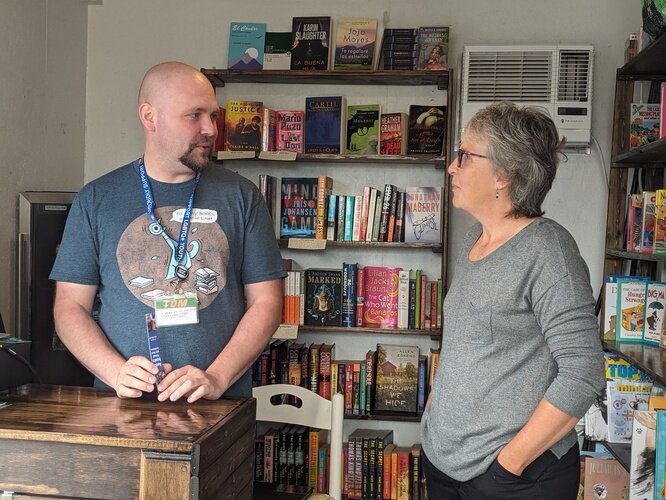 Tom Batterson and customer Laura Webb chat together inside his cargo container store, New Story Community Books.  