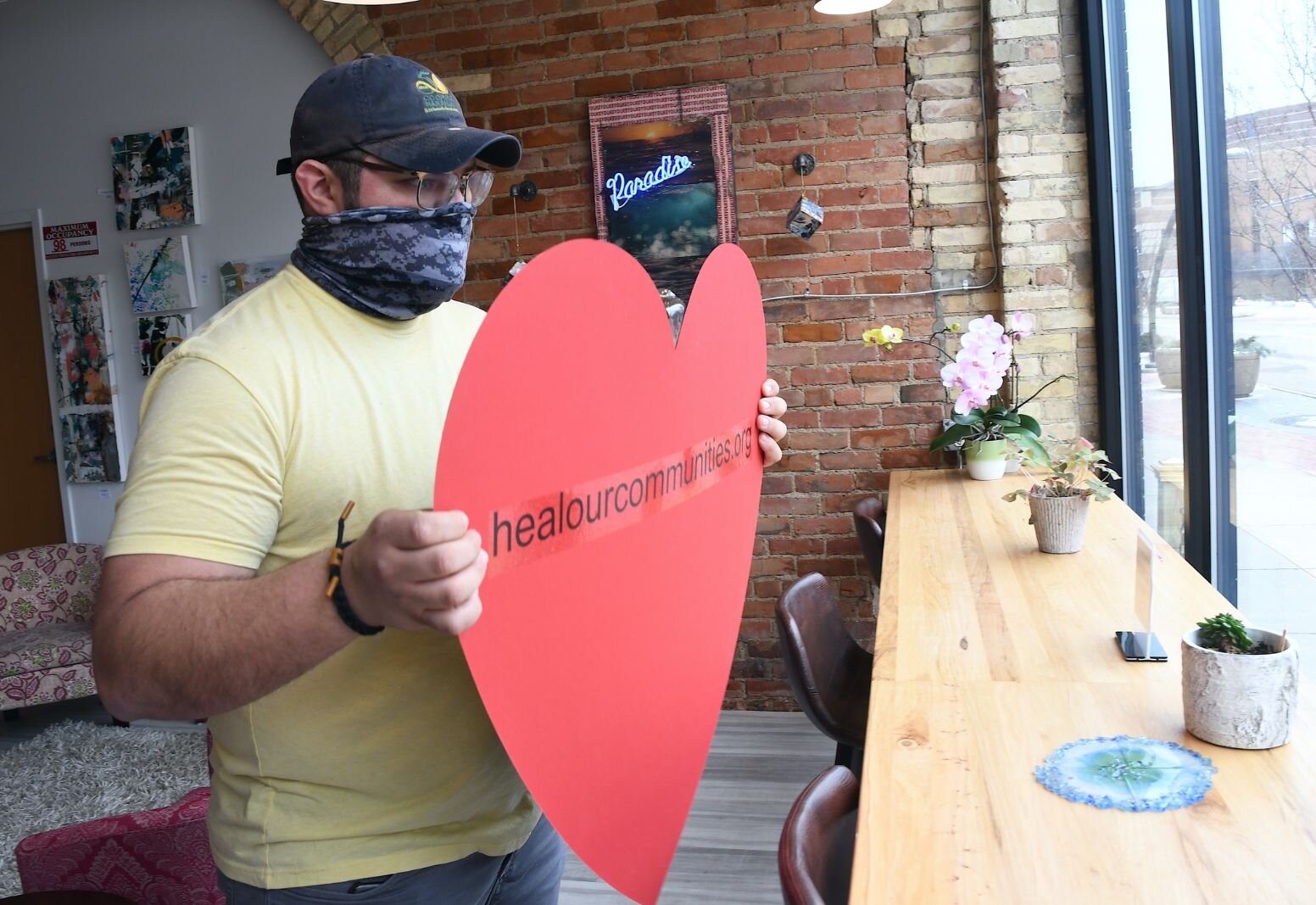 Tristan Bredehoft puts up a heart in the front window of Cafe Rica. As part of National Day of Racial Healing activities in Battle Creek on Tuesday, volunteers held and put up red hearts symbolizing  the commitment to work to end racism.