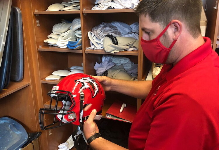 Paul Balk, an assistant coach on the Paw Paw High School football team, applies the new Red Wolves decal to a football helmet before the first football game of the year in September. 