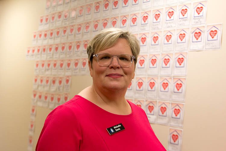 Michelle Davis stands before a wall of hearts that represent those HRI has helped stay in their homes.