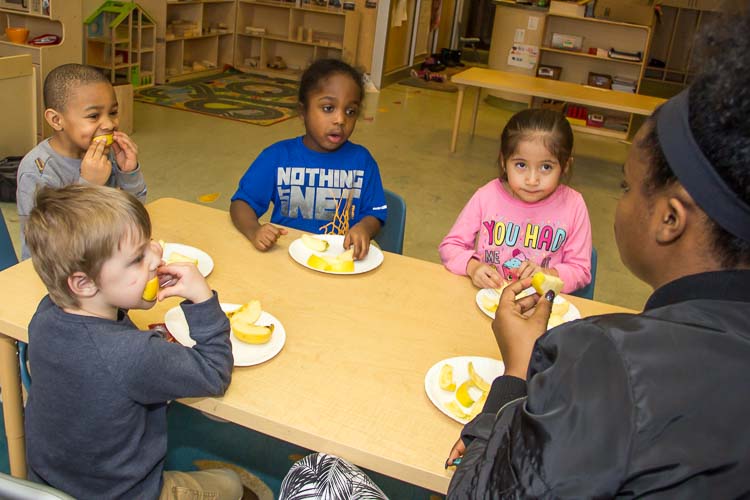 Nina Smith and children in the YWCA Children's Center eat an apple for a snack. Photo by Susan Andress