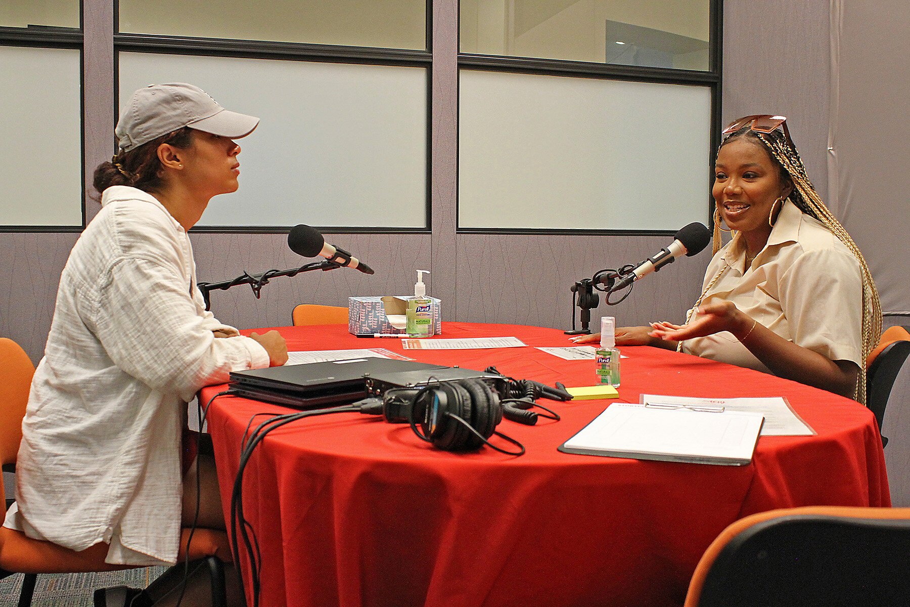 StoryCorps Manager Franchesca Peña (left) and Facilitator Shira Smillie demonstrate how a recording session at the library looked. In an actual session the facilitator sat at the table end wearing the headphones.