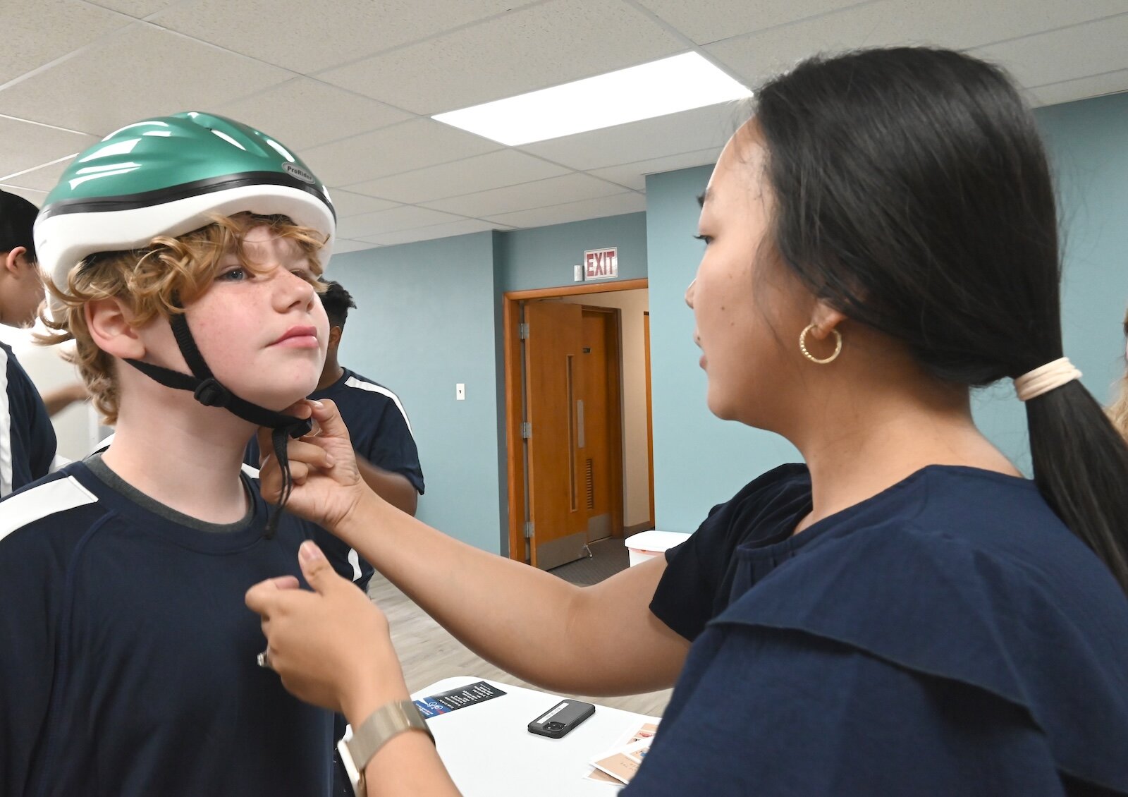 Avery Erskine gets help from Christina Swanset to properly wear a bicycle helmet.