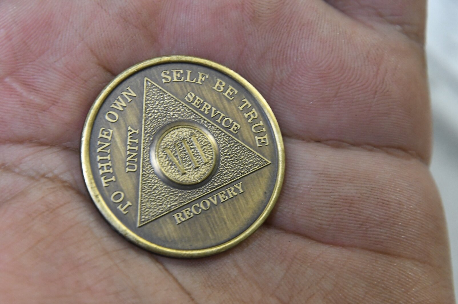 An AA member at the Pine Creek Reservation holds a coin illustrating some of the tenants of Alcoholics Anonymous.