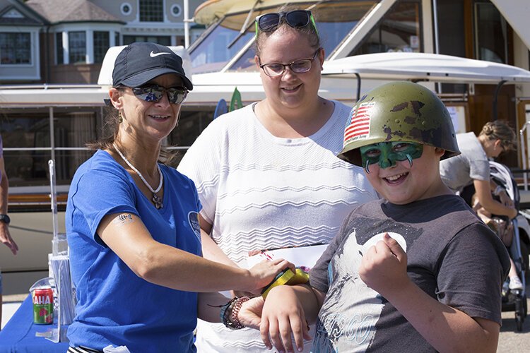 While attending the Boat the Blue Antique & Classic Boat Show, Jolene Willis (middle) and Gavin Willis (right) stopped by the Friends of the St. Clair River's booth at the event. Christy Ellery applies a temporary tattoo to Gavin's arm.