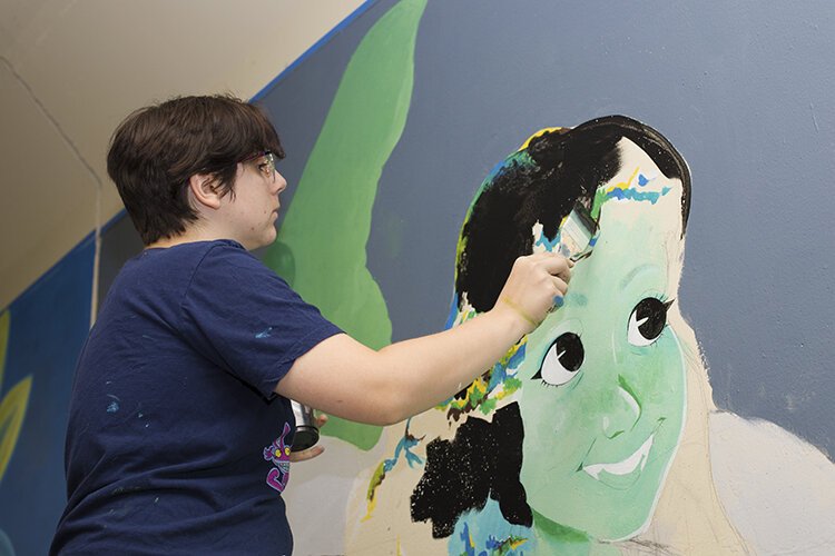 Artist Maya LePoirs focuses on painting the hair of the character featured in her mural.