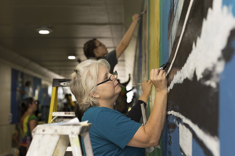 Artist Mary-Beth Fleury works on her mural depicting a ship named Manitou.
