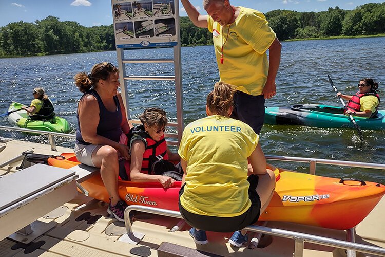 Volunteers help participants at an accessible kayak launch.