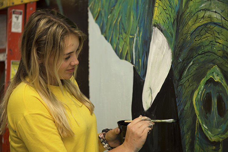Artist Grace Barrett's works on her mural depicting an elephant created using colors such as blue, green, and yellow.