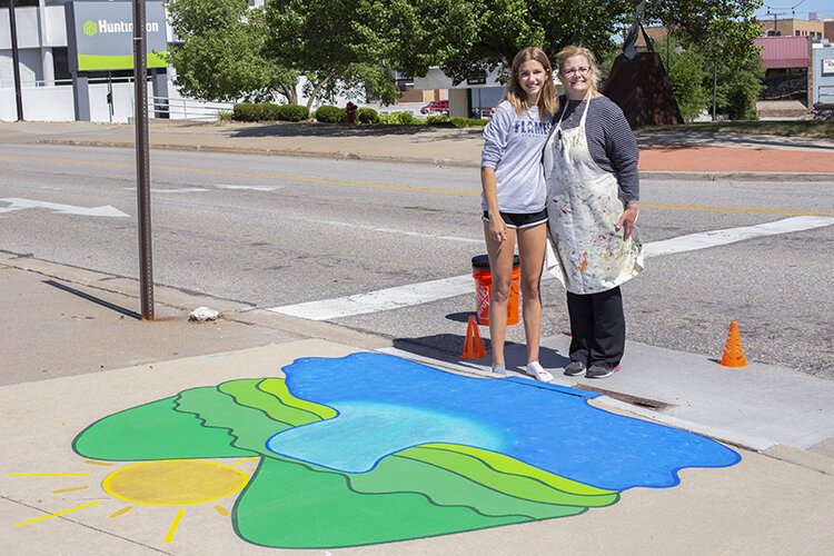 Artists Kayla Faust (left) and her mentor for the storm drain art project, Donna Mitchell-Collins, pose for a photo by Faust's artwork in downtown Port Huron.