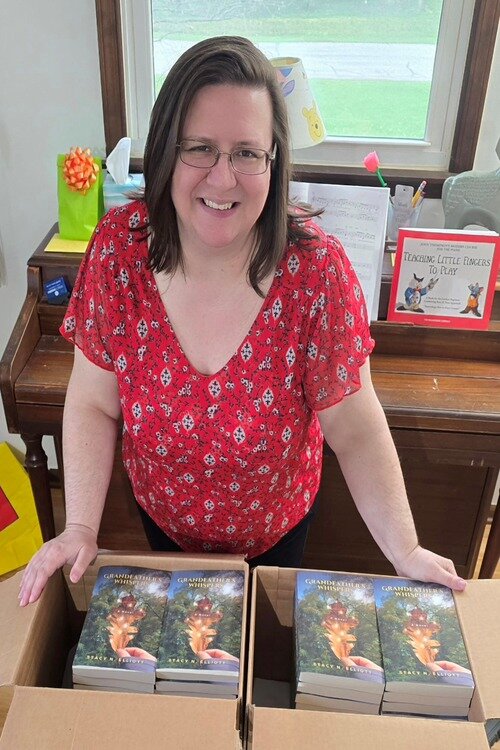 Stacy Elliott posing with boxes filled with her book Grandfather's Whispers set to release on August 1, 2024.