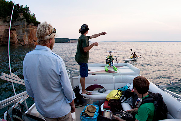 Clear & Cold Cinema member Dan Englund, pointing, directs kayakers during aerial filming on Lake Superior